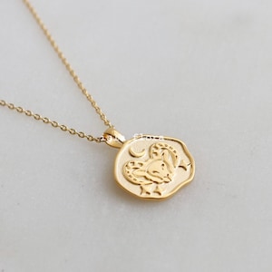 May include: A gold chain necklace with a gold pendant featuring a zodiac symbol of a ram. The pendant is detailed with a crescent moon and stars.
