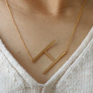 May include: A gold chain necklace with a large, open, gold letter H pendant.