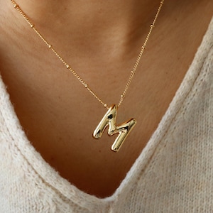 May include: A gold chain necklace with a chunky, gold, letter 'M' pendant.