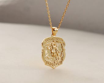 May include: A gold-toned necklace featuring a shield-shaped pendant with an embossed figure of Saint Michael. The pendant is suspended from a delicate gold-toned chain. The text Saint Michael is engraved at the top and Pray For Us at the bottom.