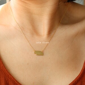May include: A gold necklace with a layered geometric pendant. The pendant is made of two rectangular shapes, one slightly larger than the other.