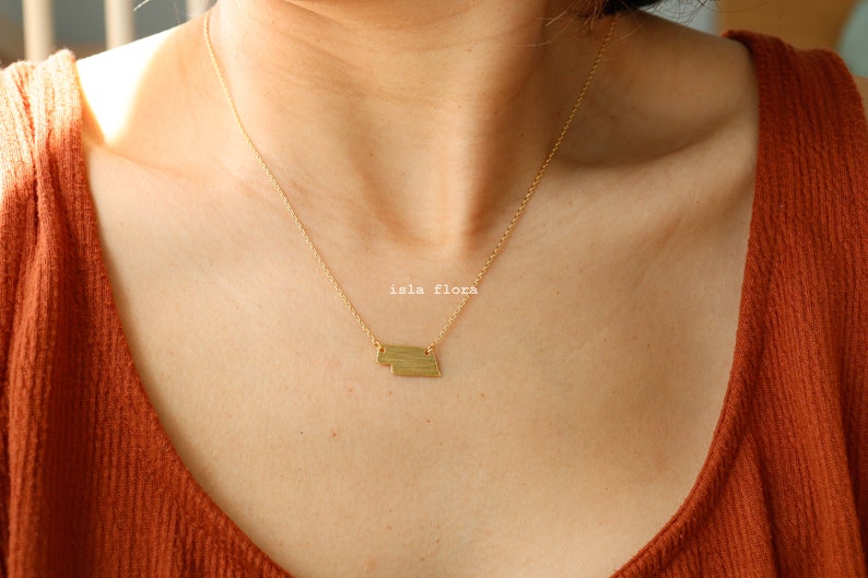 May include: A gold necklace with a layered geometric pendant. The pendant is made of two rectangular shapes, one slightly larger than the other.