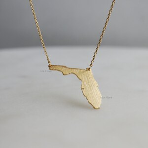 May include: Gold necklace featuring a brushed gold pendant in the shape of the state of Florida.