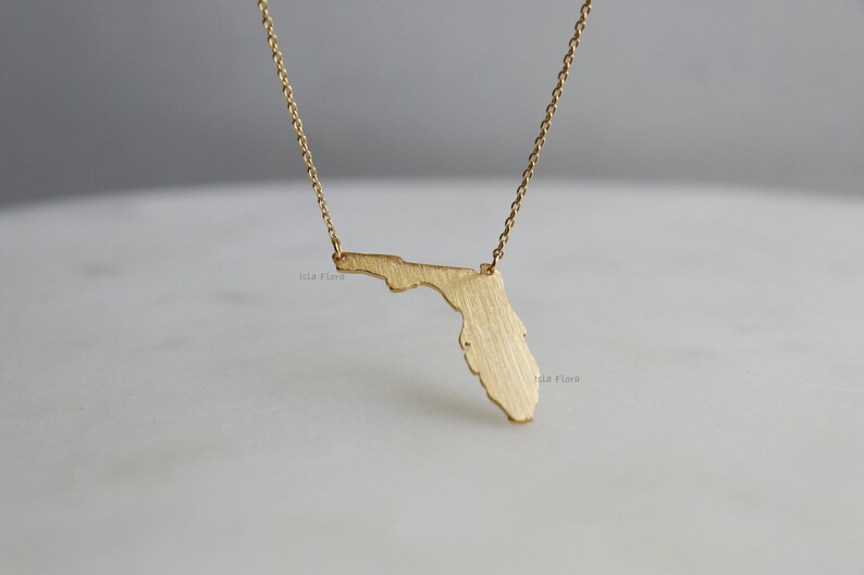 May include: Gold necklace featuring a brushed gold pendant in the shape of the state of Florida.