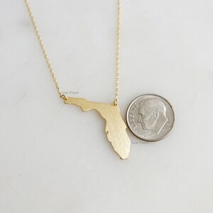 May include: Gold necklace featuring a brushed gold pendant in the shape of the state of Florida. The pendant is about the size of a US dime.