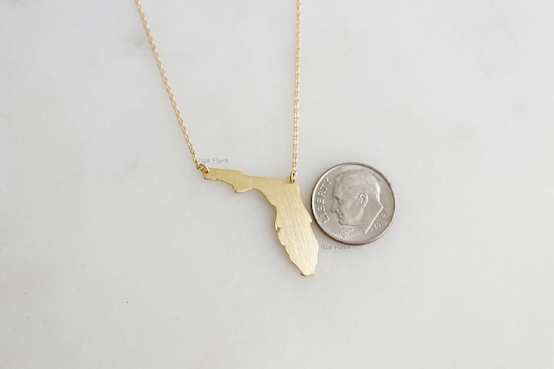 May include: Gold necklace featuring a brushed gold pendant in the shape of the state of Florida. The pendant is about the size of a US dime.