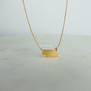 May include: A gold chain necklace with a brushed gold pendant in the shape of a rectangle. The pendant has a slightly irregular shape.