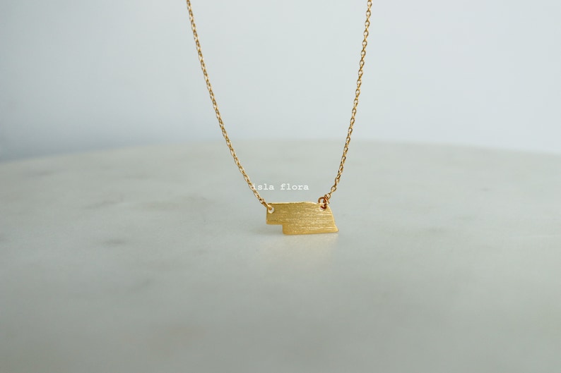 May include: A gold chain necklace with a brushed gold pendant in the shape of a rectangle. The pendant has a slightly irregular shape.