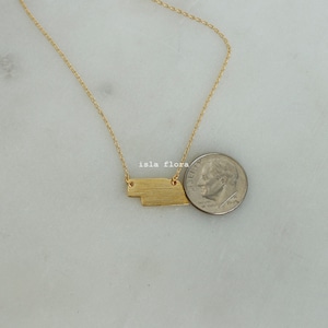 May include: A gold necklace with a geometric pendant, shown next to a US dime for size comparison.