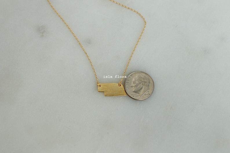 May include: A gold necklace with a geometric pendant, shown next to a US dime for size comparison.