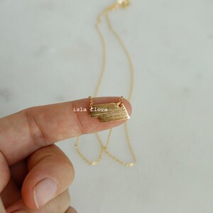 May include: A gold necklace with a textured rectangular pendant. The pendant has a slightly irregular shape.