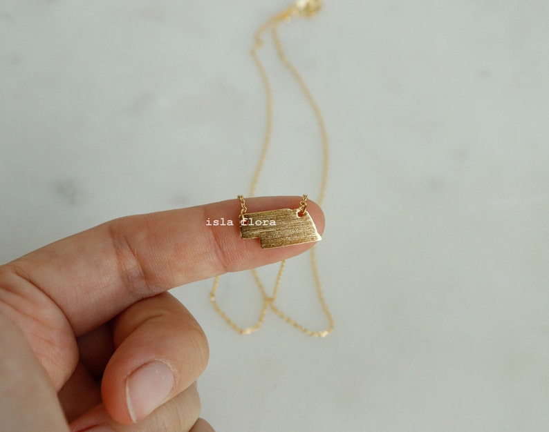 May include: A gold necklace with a textured rectangular pendant. The pendant has a slightly irregular shape.
