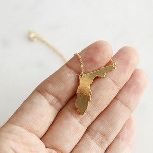 May include: Gold necklace featuring a pendant shaped like the state of Florida.