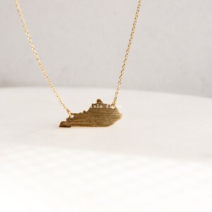 May include: A gold necklace with a pendant shaped like the state of Kentucky. The pendant has a brushed finish.