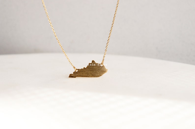 May include: A gold necklace with a pendant shaped like the state of Kentucky. The pendant has a brushed finish.