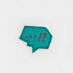 May include: A teal blue felt speech bubble with red embroidered dots and the text "...!?"