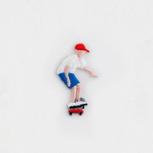 May include: Embroidered patch of a person wearing a red hat and blue shorts, skateboarding.