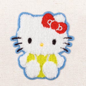 May include: A white cat-shaped embroidered patch featuring a red bow, black eyes, a yellow nose, and black whiskers. The character wears a bright yellow outfit with thin straps, all outlined in a light blue border on a textured white fabric background.