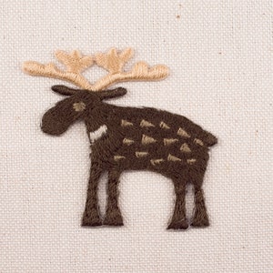 以下が含まれることがあります： ベージュの角を持つ、刺繍された茶色のヘラジカのアップリケ。ヘラジカは4本の足で立っており、模様のある体をしている。