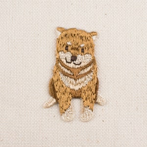 May include: Embroidered patch of a brown and white dog sitting with its paws crossed. The dog has a friendly expression and is looking directly at the viewer.