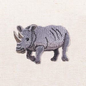 以下が含まれることがあります： 左を向いた灰色のサイの刺繍ワッペン。動物の形を定義するために詳細なステッチが施されており、目立つ角、質感のある皮膚、4本の脚が表現されています。無地のオフホワイトの布地を背景にしています。