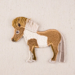Pode incluir: Um remendo de cavalo bordado em marrom e branco com uma juba e cauda marrons.