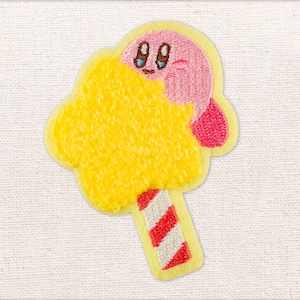 May include: Embroidered patch featuring a pink character with blue eyes emerging from a yellow cloud-like shape. The patch has a red and white striped stick, all outlined in yellow.