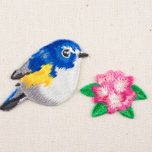 Op de afbeelding: Geborduurde strijk-op patch met een blauwe en gele vogel met een roze bloem.