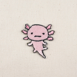 Może przedstawiać: Różowa haftowana łatka z aksolotlem z czarnymi konturami. Axolotl ma mały grymas na twarzy.