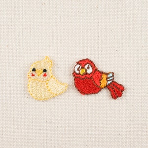 May include: Two embroidered iron-on patches featuring a yellow bird and a red bird. The yellow bird has a round body and a small beak. The red bird has a round body and a small beak. Both birds have black eyes.