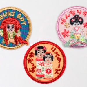 May include: Three embroidered patches with Japanese-themed designs. One patch features a Kabuki Boy with red hair and the text "KABUKI BOY". Another shows a geisha with floral accents. The third patch depicts two figures in traditional attire.
