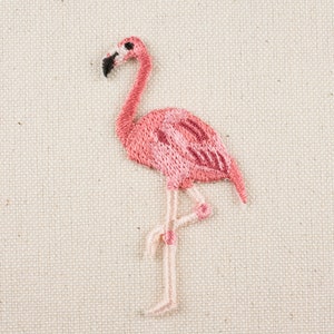 May include: Pink embroidered flamingo with a black eye and a white background.