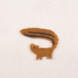 May include: Embroidered brown squirrel with a long, curled tail. The squirrel is outlined in black thread.