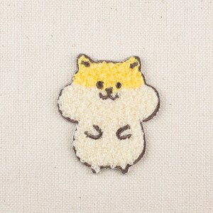 May include: A white and yellow embroidered patch of a hamster with a brown outline.