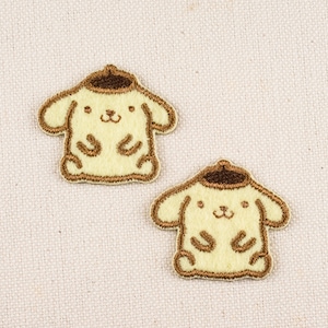 May include: Two embroidered patches featuring a cartoon character with a light yellow body, brown hat, and brown outline. The patches are on a light beige fabric background. The character has a smiling face and small arms and legs.