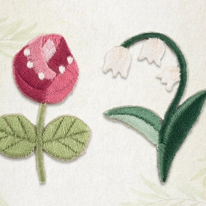 Op de afbeelding: Twee geborduurde stoffen bloemenpatches. De eerste patch is een roze en witte bloem met groene bladeren. De tweede patch is een witte lelie met groene bladeren.
