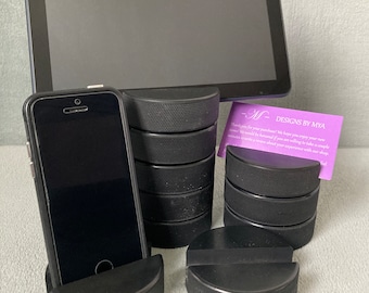 May include: A set of black hockey puck phone and tablet stands. The stands are made of stacked hockey pucks. A business card with the text " -M- DESIGNS BY MYA" is in the image.  Thank you for your purchase! We hope you enjoy your new item! It would be an honor if you are willing to take a couple minutes to write a review about your experience with our shop!"