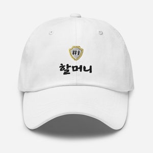 May include: White baseball cap with a gold shield with the number 1 inside and the text "#1 챔피언" in black.