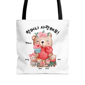 May include: White tote bag with a brown bear holding a red heart that says "For You" and a cupcake that says "Love". The bear is wearing a flower crown and surrounded by four smaller bears with the names Amy, Ben, Ava, and Nat.