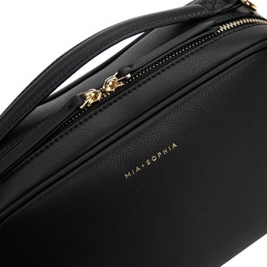 May include: Black leather crossbody bag with a gold zipper and the text "MIA + SOPHIA" on the front.
