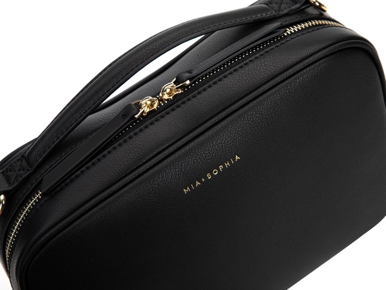 May include: Black leather crossbody bag with a gold zipper and the text "MIA + SOPHIA" on the front.