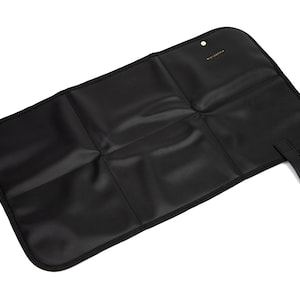 May include: Black changing mat with a fold-over design and a small strap. The mat has five sections and is made of a water-resistant material.