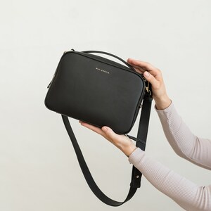 May include: A black leather crossbody bag with a gold strap and the text "MIA + SOPHIA" on the front.
