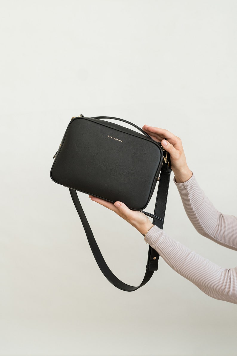 May include: A black leather crossbody bag with a gold strap and the text "MIA + SOPHIA" on the front.
