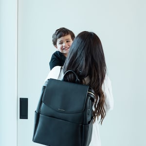 May include: A black leather diaper bag backpack with gold accents and the word "MILKBARN" printed on the front.