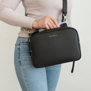 May include: A black leather crossbody bag with a gold zipper and a gold strap. The bag has the text "MIA + SOPHIA" printed on the front.