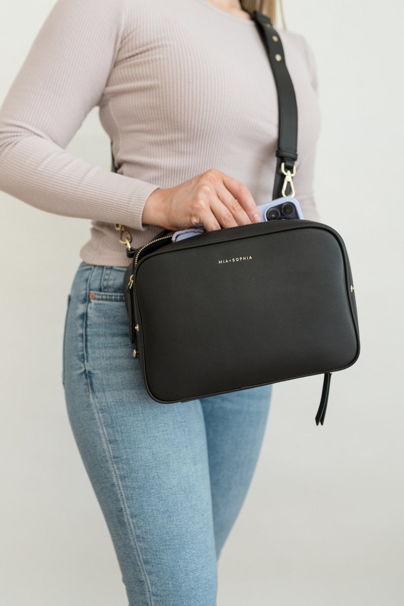May include: A black leather crossbody bag with a gold zipper and a gold strap. The bag has the text "MIA + SOPHIA" printed on the front.