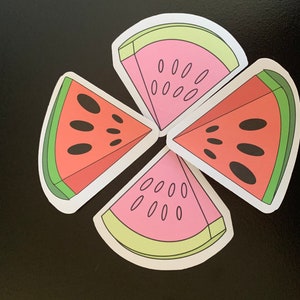 Puede incluir: Cuatro pegatinas con forma de rodajas de sandía dispuestas en un patrón circular. Cada pegatina presenta un interior rosa, semillas negras, una corteza verde y un borde blanco. Las pegatinas están sobre una superficie negra.