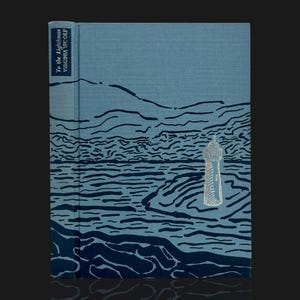 May include: A hardcover book titled To the Lighthouse by Virginia Woolf with a blue fabric cover. The front features a dark blue abstract line illustration of a landscape and sea, with a prominent silver foil lighthouse graphic on the right.