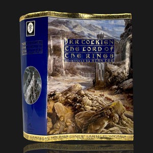 May include: A hardcover book titled The Lord of the Rings by J.R.R. Tolkien, illustrated by Alan Lee. The cover features a detailed landscape painting with rocky terrain, a tall tower, and figures. The spine is deep blue with gold lettering.